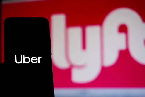 11 décembre 2019. Dans cette illustration photo, le logo Uber est affiché sur un smartphone et le logo Lyft sur le fond flou — Photo