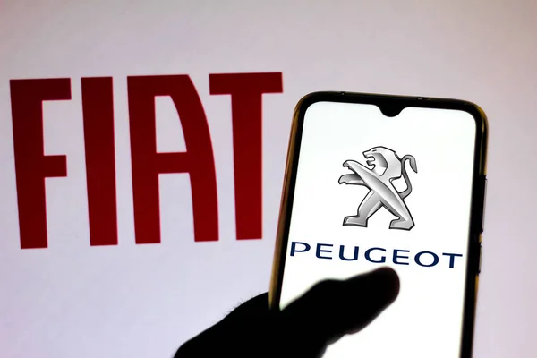 19 грудня 2019, Бразилія. На цьому фото зображено логотип Peugeot на смартфоні і логотип Fiat Automobiles на розмитому фоні — стокове фото