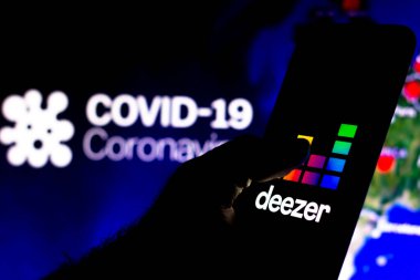 8 Nisan 2020, Brezilya. Bu resimde Deezer logosu arka planda COVID-19 Coronavirus 'un bilgisayar modeli ile akıllı bir telefonda görüntülendi..