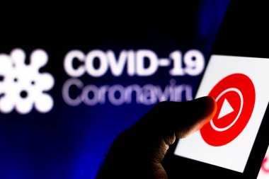 8 Nisan 2020, Brezilya. Bu resimde, Youtube Play logosu arka planda COVID-19 Coronavirus 'un bilgisayar modeli olan bir akıllı telefonda görüntülendi..