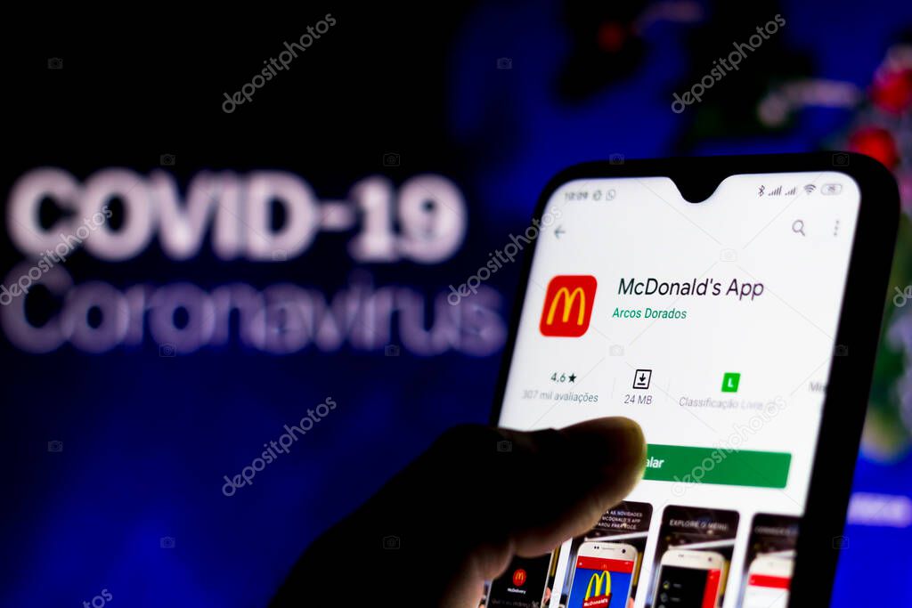 April 8, 2020, Brazil. In this photo illustration the McDonalds logo seen displayed on a smartphone with a computer model of the COVID-19 coronavirus in the background.