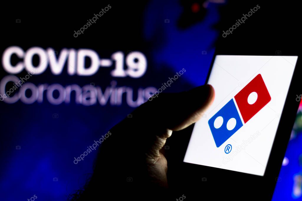 April 8, 2020, Brazil. In this photo illustration the Dominos Pizza logo seen displayed on a smartphone with a computer model of the COVID-19 coronavirus in the background.