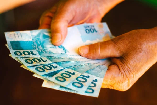 Retired woman checks notes of one hundred reais (600 reais). Money from Brazil and minimum wage concept and government aid.