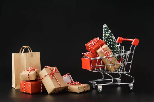 Carro de compras lleno de varias cajas de regalo y un árbol de Navidad . — Foto de Stock