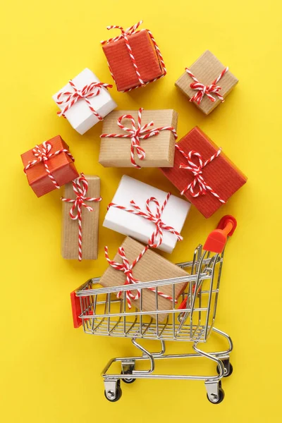 Winkelwagen vol geschenkdoosjes op gele achtergrond. — Stockfoto