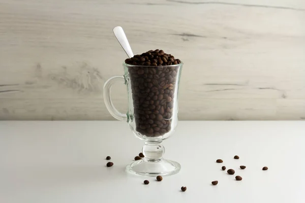 Una taza de vidrio está llena de granos de café. Fondo claro, orientación horizontal — Foto de Stock