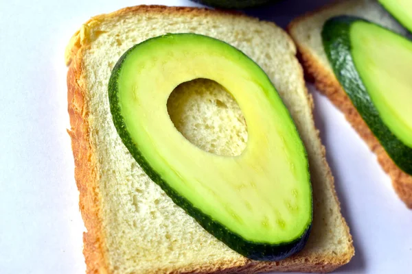 Sliced green avocado slices with a sandwich on a white background