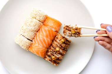 A girl holds a roll with chopsticks.