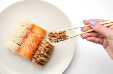 A girl holds a roll with chopsticks.
