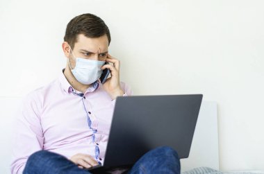 Coronavirus. Karantinaya alın. Gömlekli ve kotlu bir adam iş sorunlarını uzaktan çözer. Maskeli olan. Belgeler. Laptop ve telefon. Dünyada koronavirüs salgını.