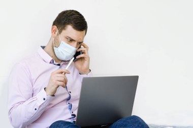 Coronavirus. Karantinaya alın. Gömlekli ve kotlu bir adam iş sorunlarını uzaktan çözer. Maskeli olan. Belgeler. Laptop ve telefon. Dünyada koronavirüs salgını.