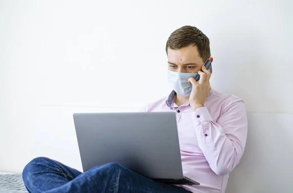 Coronavirus 一个穿衬衫和牛仔裤的男人远程解决工作问题 戴着面具文件 笔记本电脑和电话 世界上的结肠炎大流行病 — 图库照片