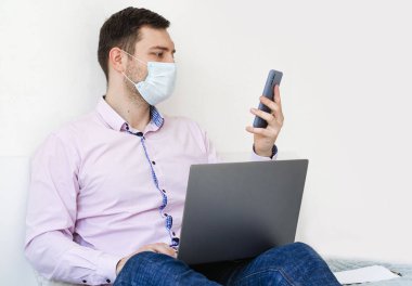 Coronavirus. Karantinaya alın. Gömlekli ve kotlu bir adam iş sorunlarını uzaktan çözer. Maskeli olan. Belgeler. Laptop ve telefon. Dünyada koronavirüs salgını.