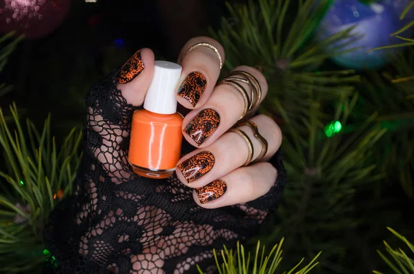 Маникюр дизайн ногтей для нового года, черные блестящие ногти с оранжевым ногтей на фоне елки — стоковое фото