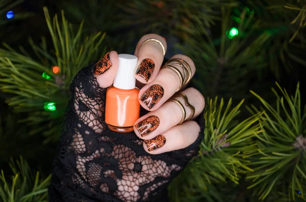 manicure nail art design for new year, black sparkling nails with orange nail art on the background of the Christmas tree
