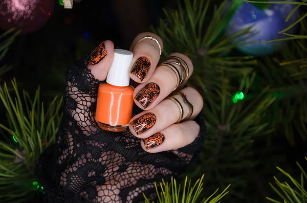 Маникюр дизайн ногтей для нового года, черные блестящие ногти с оранжевым ногтей на фоне елки — стоковое фото