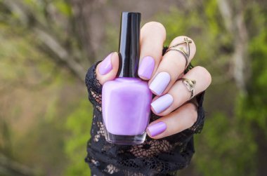 Kadın elinde oje şişesi tutuyor. Güzel eller. Doğal yeşil arka planda Moda Moda Moda Moda Renkli Tırnakları. Kısa salon tırnakları.