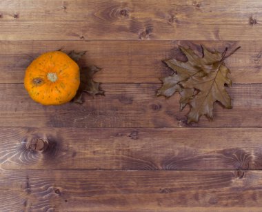 Kahverengi ahşap arka planda yaprakları olan turuncu sonbahar balkabağı. Cadılar Bayramı konsepti, fotokopi alanı olan üst görünüm.