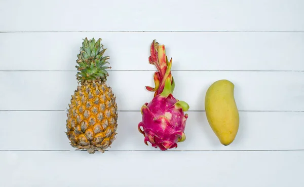 Exotic asia fruits on white wood background. Assorted tropical summer fruits. Mango, dragon fruit, pitahaya and pineapple. Top view fresh fruit flat lay.