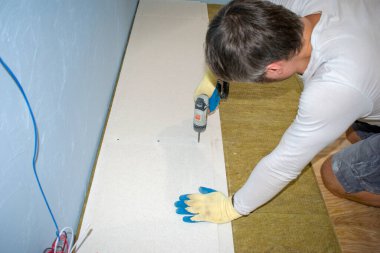 Laying the floor in the apartment. Stone wool for the floor. Sound insulation of floors for the national tie. A man is drilled with a tool gypsum-fiber plates. clipart