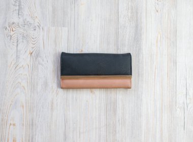 Ahşap arka planda izole edilmiş doğal deri bir kadın cüzdanı. Mıknatısta kadın çantası siyah ve bej rengi.