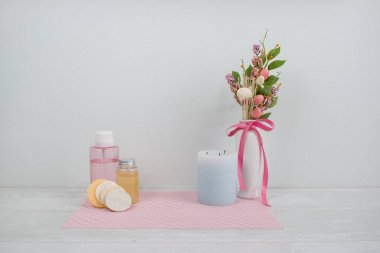 Bir evin iç dekorasyonu ve güzellik seti ürünleri, süngerler, losyon, krem. Beyaz ahşap arka planda peçete, çiçekler, aroma mumu ve beyaz vazo. Modern iç mekan. Minimalizm tarzı.