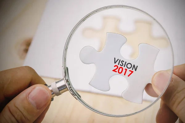 Hand with magnifying glass looking at a piece of jigsaw puzzle — Stock Photo, Image