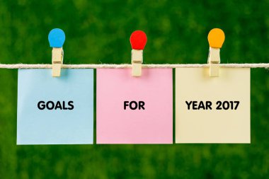 Yeşil arka plana karşı bir ip tarafından asılı renkli yapışkan renk kağıtları.