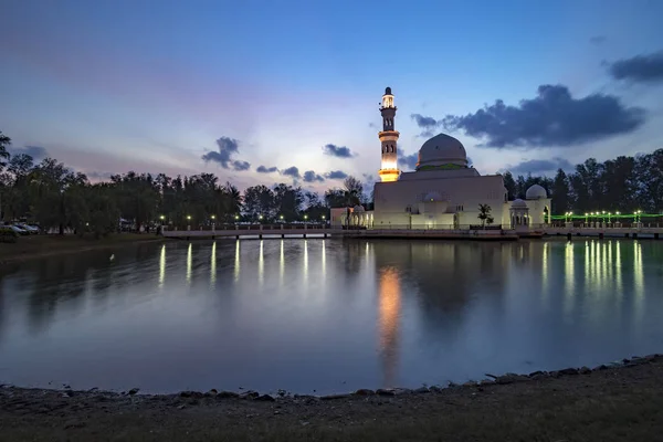 Beautiful white mosque by the lakeside during sunrise with reflection on the lake in Terengganu, Malaysia.