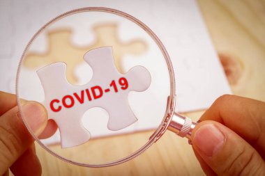 Elinde büyüteçle Covid-19 kelimeleriyle kayıp yapboz parçalarını arıyor..