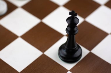 Kahverengi ve beyaz satranç tahtasında satranç saati olan siyah ve beyaz plastik satranç taşları.