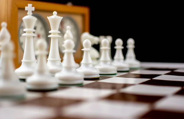 Kahverengi ve beyaz satranç tahtasında satranç saati olan siyah ve beyaz plastik satranç taşları.