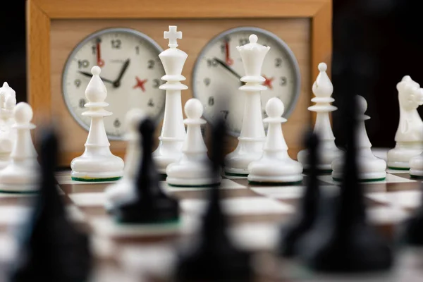 Kahverengi ve beyaz satranç tahtasında satranç saati olan siyah ve beyaz plastik satranç taşları.