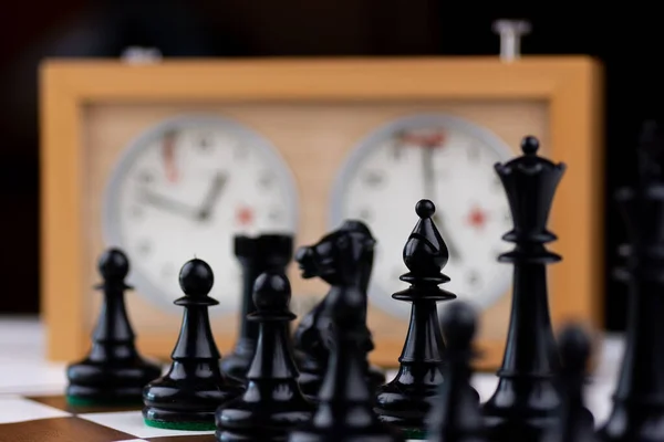 Kahverengi ve beyaz satranç tahtasında satranç saati olan siyah ve beyaz plastik satranç taşları.
