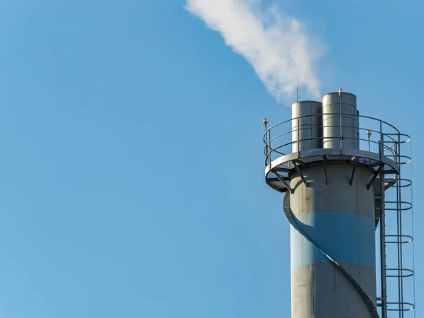 La cheminée fumante de l'entreprise contre le ciel bleu . — Photo