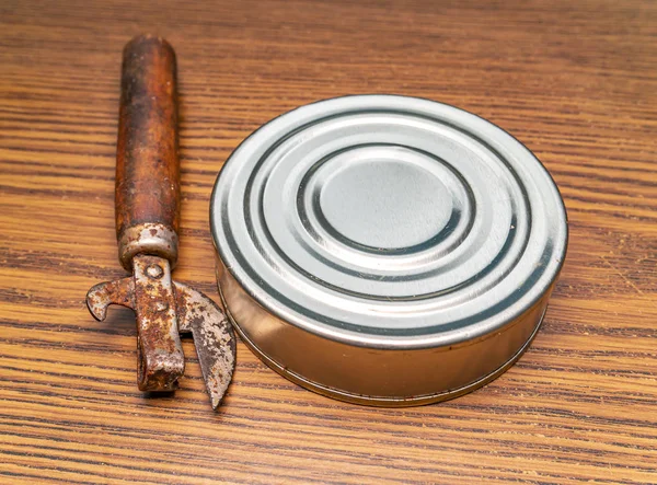 Tin can and can opener on a wooden table.