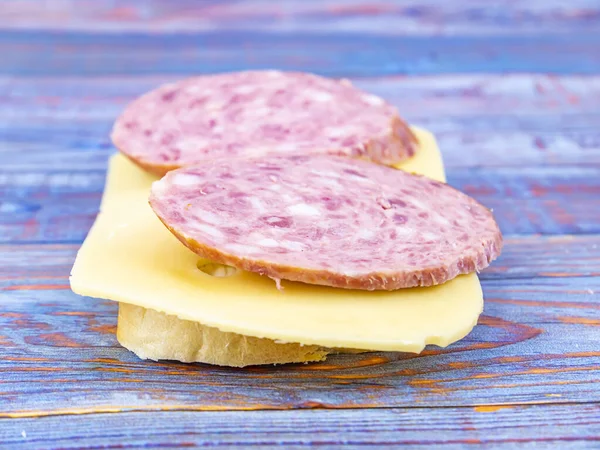 Fazer um sanduíche com salsicha e queijo duro em uma tábua de corte . — Fotografia de Stock