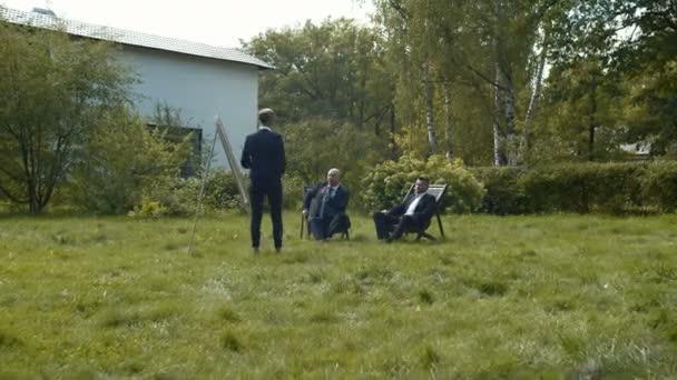 Двое мужчин сидят во дворе и разговаривают с женщиной. . — стоковое видео