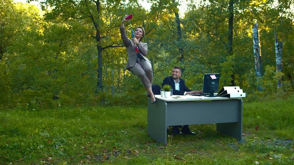 A férfi az asztalnál dolgozik, a nő a kötélen repül és szelfit készít.. — Stock Fotó