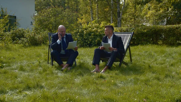 Мужчины в костюмах сидят во дворе с бумагами и разговаривают . — стоковое фото