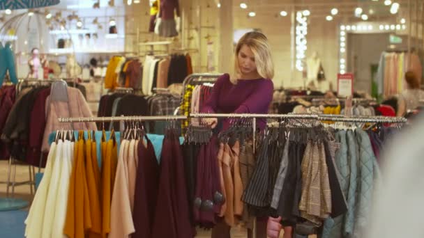 Frau sortiert Sachen auf Kleiderbügel im Geschäft — Stockvideo
