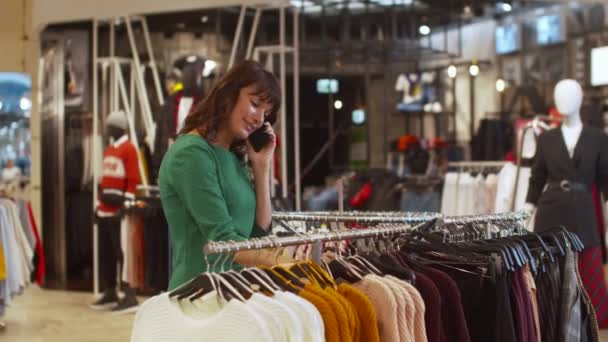 Mujer agradable elige un suéter y habla por teléfono con entusiasmo — Vídeo de stock