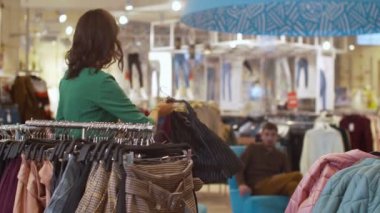 Kadın şort ve süveteri seçerken, erkek telefonda konuşuyor.