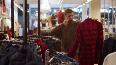 Adam elbiselerini seçiyor ve telefonda konuşuyor. 