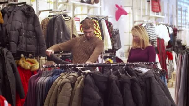 Mujer joven ayuda a su hombre a elegir una chaqueta — Vídeos de Stock