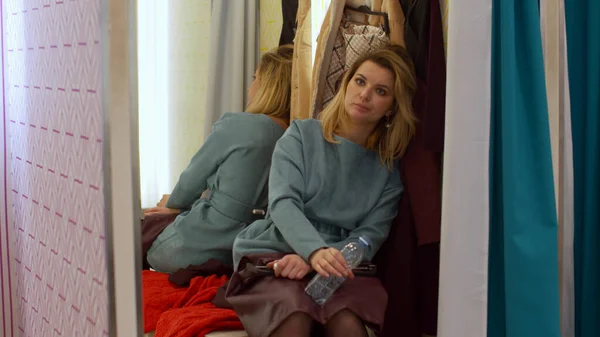 Tired girl is sitting in the fitting room and drinking water — Stock Photo, Image