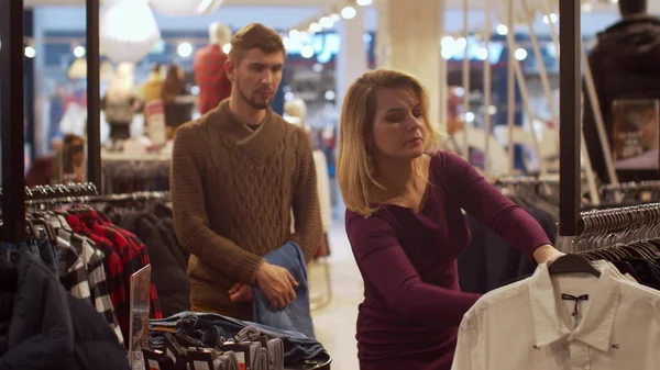 Красивая женщина выбирает своему мужчине рубашку в магазине — стоковое фото