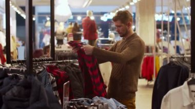 Genç adam bir mağazada kıyafet arıyor.