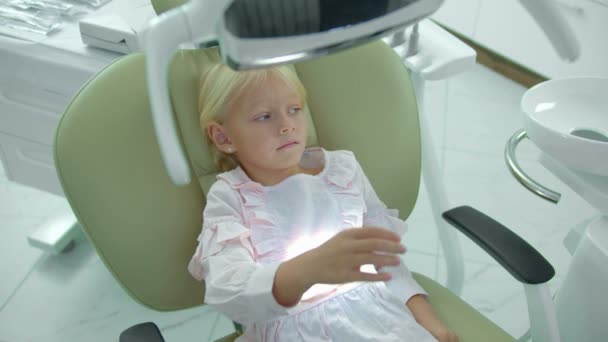 Linda chica se sienta en la silla del dentista, apaga una lámpara — Vídeo de stock