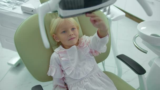 Dziewczyna siedzi na krześle dentystycznym, wyłącza się i na lampie — Wideo stockowe